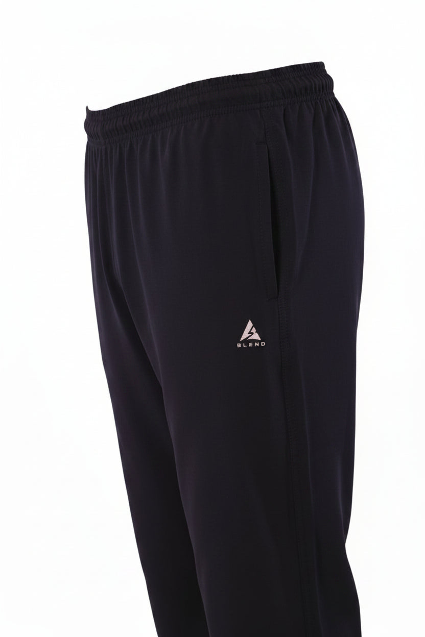 A professional e-commerce product photograph based on the provided black track pants w/ side piping. Present the garment as a flawless ghost mannequin view, appearing hollow and complete on an invisible form. Remove all visible skin and mannequin parts (torso and feet). Smooth out all wrinkles and creases from the fabric while preserving the texture. Retain and sharpen the double white piping along the side seam and the silver triangular 'A' logo on the left thigh. The background is a seamless, pure white.